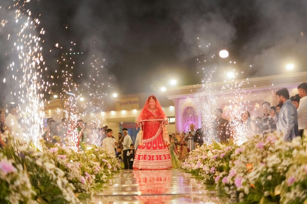 A beautiful Indian bride in traditional attire walking down the aisle surrounded by fireworks in Delhi.