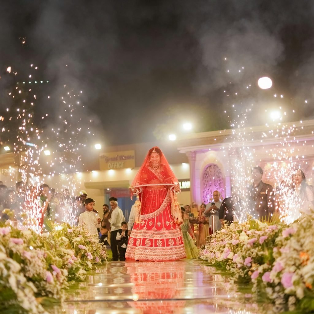 A beautiful Indian bride in traditional attire walking down the aisle surrounded by fireworks in Delhi.